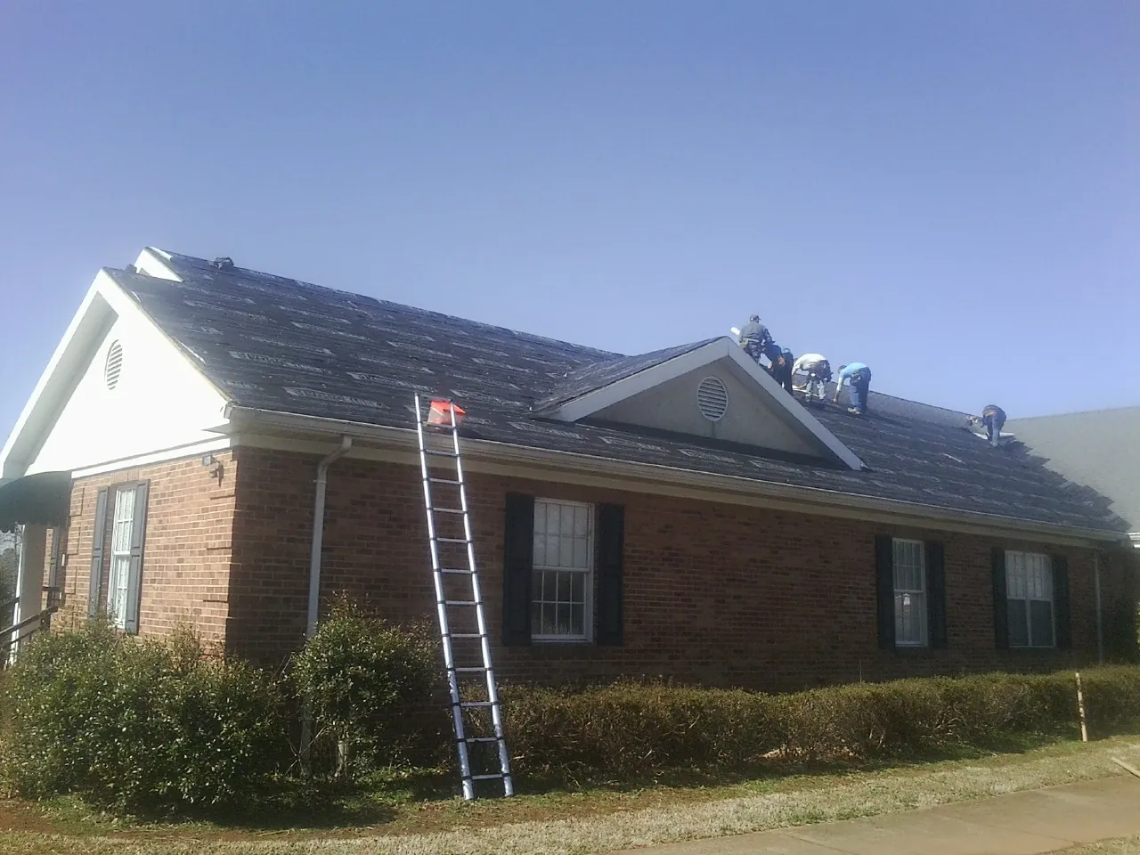 Crew tearing shingles off a brick ranch roof with a ladder set — Metal Roof Repair work by our crew in Plant City