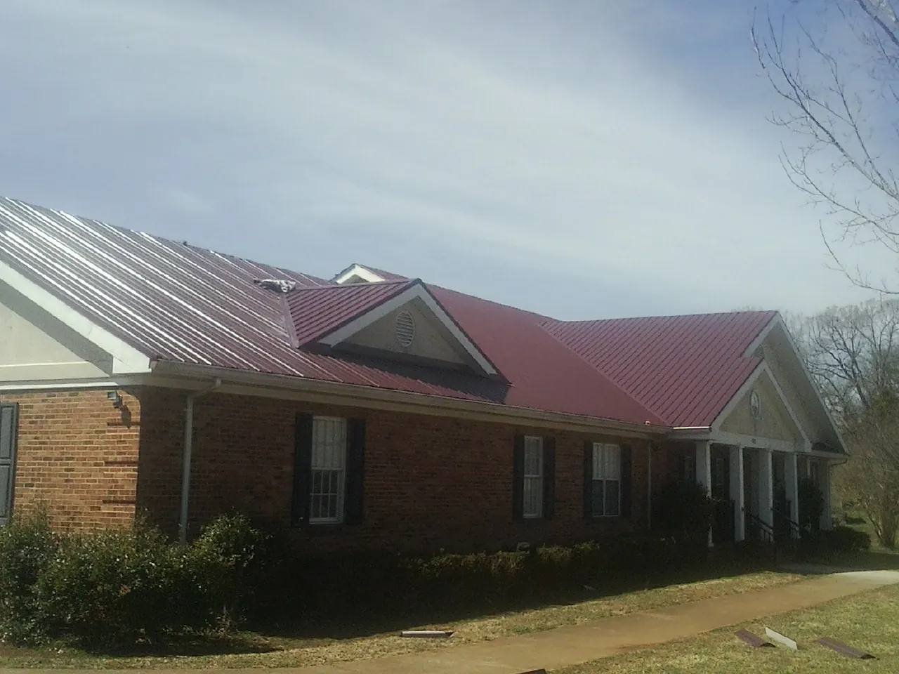 Red metal roof with gabled entries on a long brick building, from a Hail Damage Roof Repair job in Plant City