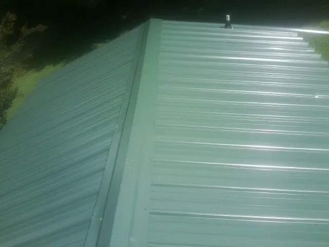 New green metal panels meeting at the ridge of a roof — Flat Roof Repair work by our crew in Plant City