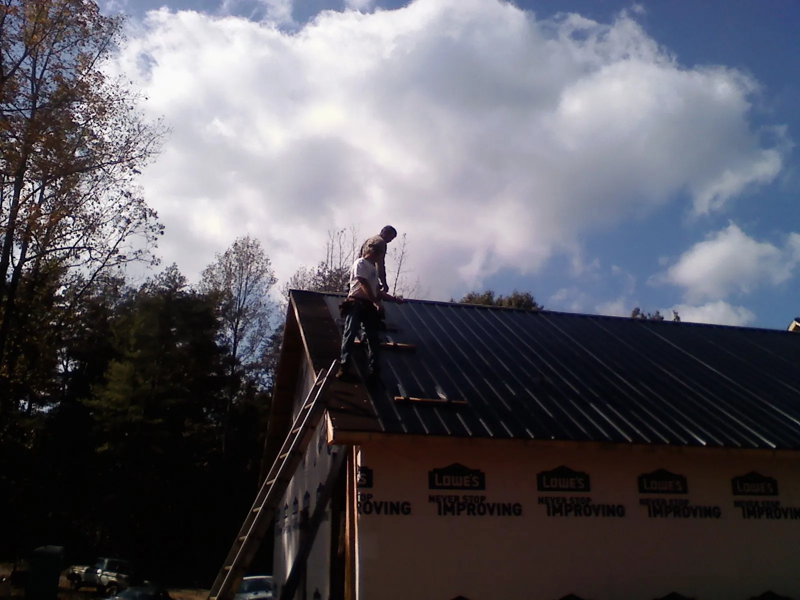 Roofer fastening dark metal panels high against a cloudy sky, from a Roof Inspection job in Plant City