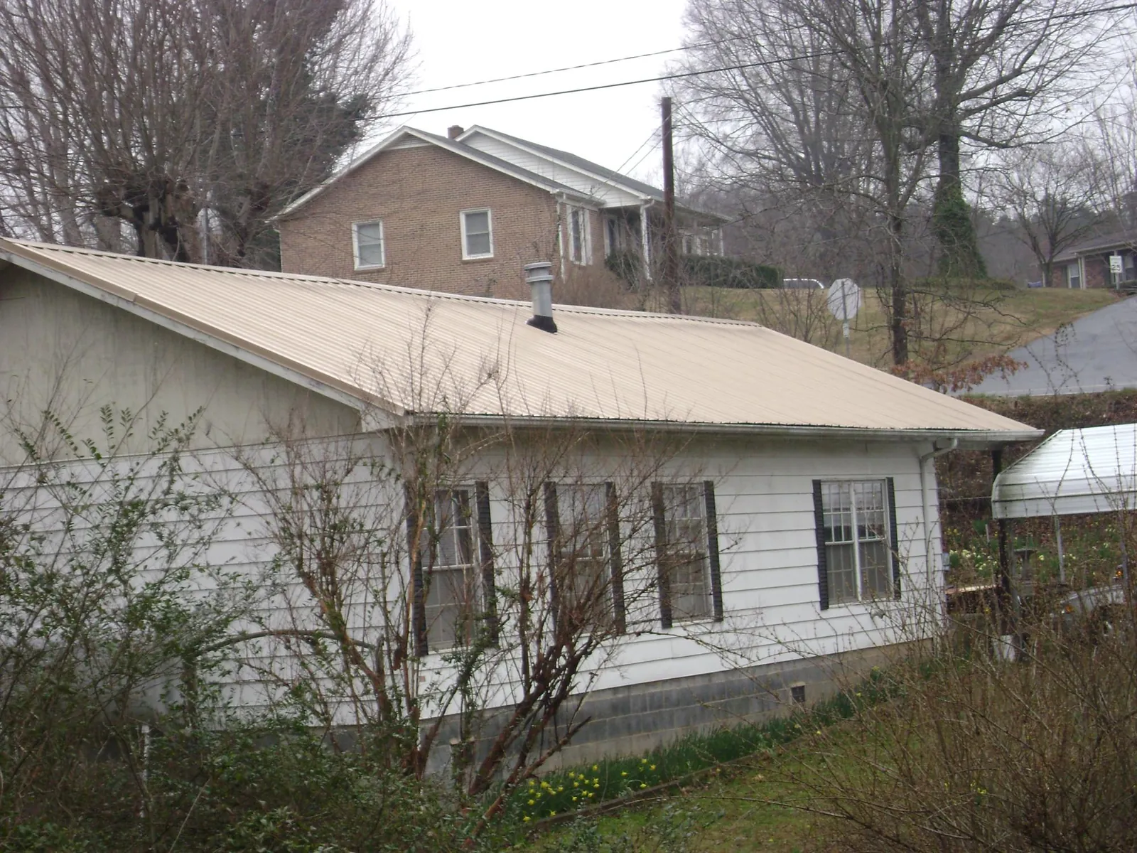 Tan metal roof on a white sided house set into a hillside — Commercial Roofing by Roofing Brothers in Plant City
